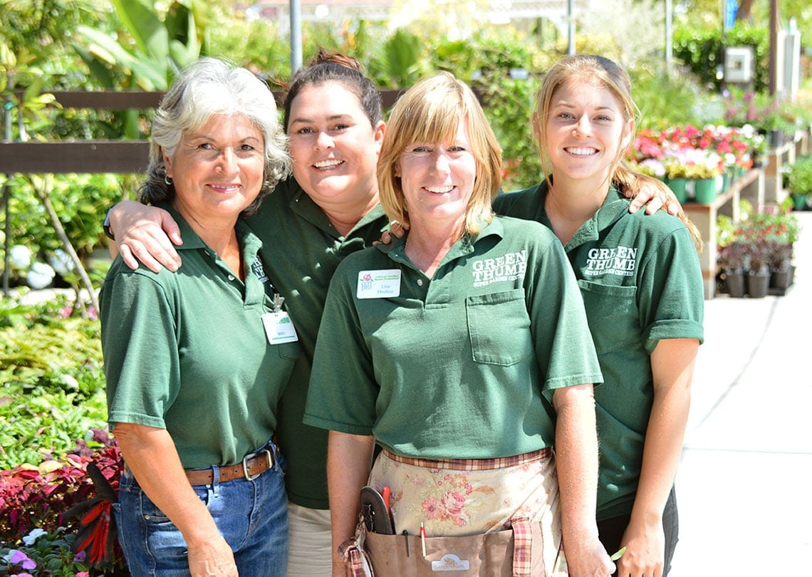 Four women in green shirts standing in front of plants.