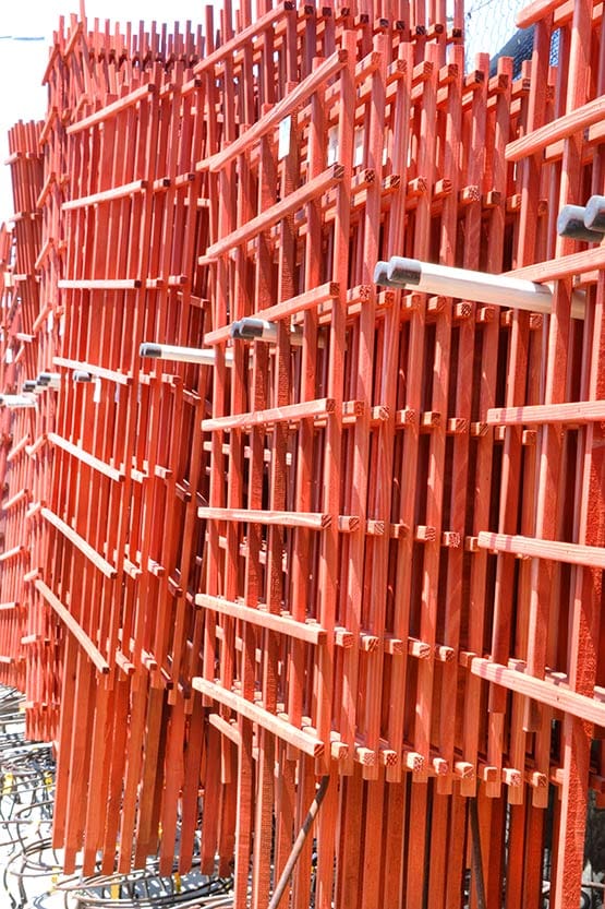 A large pile of red wooden beams on a construction site.