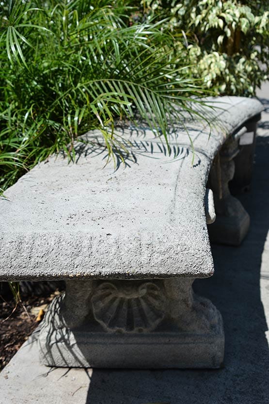 A bench is sitting on a sidewalk next to a plant.